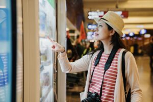 Finding the right vending machine location can make all the difference. A traveling woman with binoculars around her neck points at the glass of a vending machine at the airport.